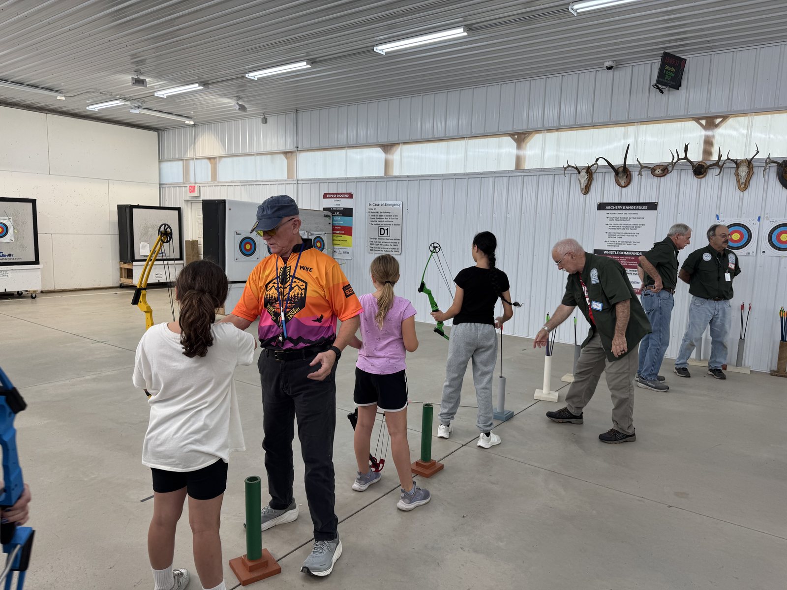 An intro class on the indoor range — a coach working with a young archer at the shooting line